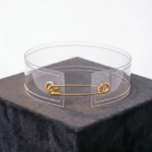 Beyaz fon üzerinde minimal tasarım çengelli iğneli şeffaf choker ile mankenin sağ yandan pozu.