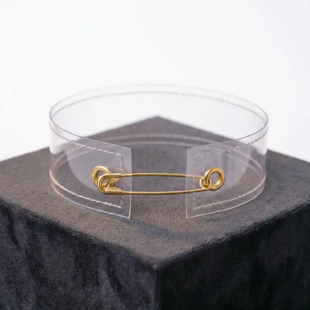Beyaz fon üzerinde minimal tasarım çengelli iğneli şeffaf choker ile mankenin sağ yandan pozu.